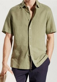 Camisa de lino de manga corta en color verde oliva con botonadura frontal, un corte relajado y una textura ligera, combinada con pantalones oscuros.