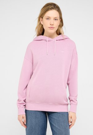 Hellrosa Kapuzenpullover aus strukturiertem Stoff, mit verstellbarer Kordel am Kapuzenrand und einer Fronttasche. Kombiniert mit blauen Jeans.