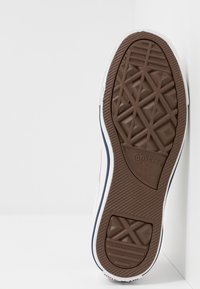 Semelle de basket Converse en caoutchouc marron avec motif texturé, bord et logo blancs ; design plat pour adhérence et durabilité.