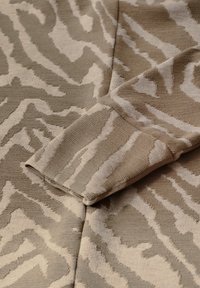 Beiger Strickstoff mit einem kontrastierenden weißen Zebra-Muster; Nahaufnahme des Ärmels mit geripptem Textur und glatter Oberfläche.