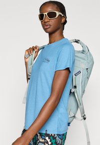 Ανοιχτό μπλε κοντομάνικο μπλουζάκι με μικρό λογότυπο Patagonia, συνοδευόμενο από γκρι σακίδιο πλάτης με ρυθμιζόμενους ιμάντες και πολλαπλές τσέπες με φερμουάρ.