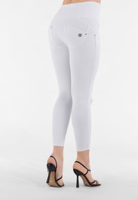 Leggings bianchi con vita alta, caratterizzati da una finitura testurizzata e tasche posteriori con accenti metallici. Abbinati a sandali neri con tacco alto.