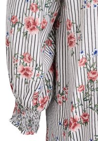 Tissu blanc avec des rayures verticales noires, orné de motifs floraux roses et bleus. Manches avec des poignets élastiques froncés.