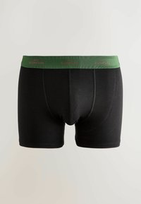 Boxeri negri pentru bărbați, cu brâu verde, având textul roșu "NEXT SIGNATURE", expuși pe un fundal neutru.