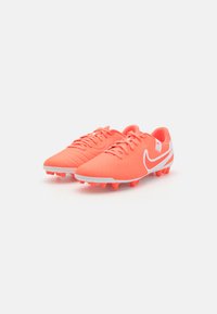 Bright coral soccer cleats with a textured synthetic upper, white accents, and conical studs for grip on turf surfaces.