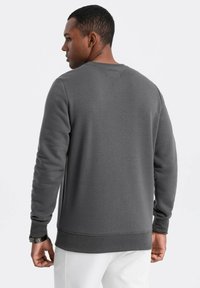 Felpa grigio scuro con tessuto testurizzato, collo rotondo e polsini a coste. Presenta un retro semplice con un piccolo etichetta sul collo.