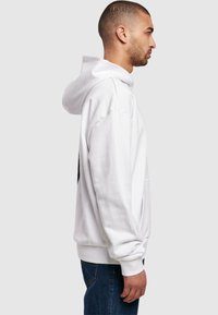Felpa bianca con vestibilità rilassata, cappuccio con cordino e polsini a coste. Materiale in cotone, dotata di una tasca frontale e design minimalista.