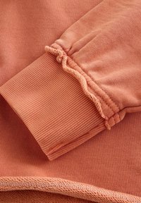 Manche de pull en coton de couleur corail douce, dotée d'une texture côtelée, d'un poignet élastique avec un détail froncé et d'un fini en tissu lisse.