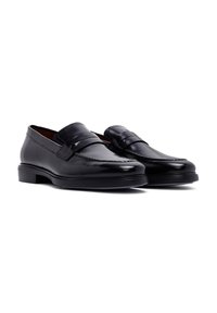 Schwarze Lederloafers mit einem gesteppten Zehen-Design, flachem Absatz und einem dekorativen Band über dem Vorderfuß. Glatte Textur und polierte Oberfläche.