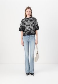 Svart-hvitt mønstret t-skjorte med korte ermer, kombinert med lyseblå vide jeans og svarte sko, holder en beige veske.