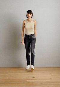 Beige ujjatlan felső, fekete karcsú farmernadrág összetett varrással és fehér tornacipő; sima anyag, szűkített fazon, a bokánál felhajtva.
