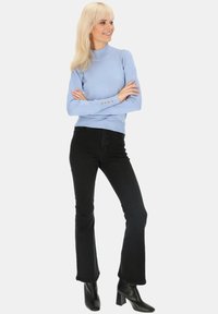 Jasnoniebieski sweter z golfem o prążkowanej teksturze i złotymi guzikami, zestawiony z czarnymi spodniami dzwonami i czarnymi botkami na obcasie.