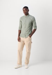 Cămașă deschis verde, cu mâneci lungi și nasturi, din bumbac. Pantaloni bej, cu croială lejeră. Adidași în culori deschise. Design minimalist.