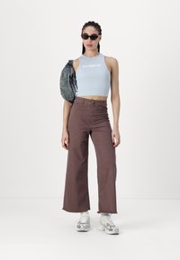 Un crop top léger bleu clair avec du texte blanc, associé à un pantalon large marron et des baskets blanches chunky. Les accessoires incluent des lunettes de soleil noires.