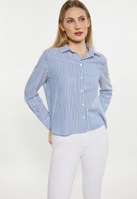 Blauw en wit gestreept overhemd met een puntige kraag en lange mouwen, gecombineerd met witte strak aansluitende broek. Glad stoffen textuur.
