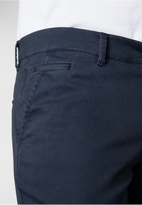 Námořnické modré chinos kalhoty s texturovanou látkou, vybavené přední kapsou, poutky na pásek a slim fit střihem. Diskrétní akcenty v podobě šití.