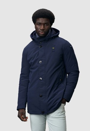 Chaqueta acolchada azul marino con capucha, que presenta grandes botones frontales, dos bolsillos laterales y un parche de logo en la manga. Textura suave.