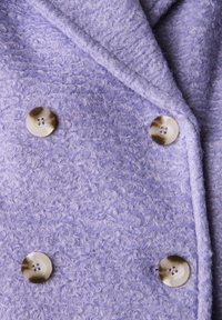 Cappotto bouclé viola chiaro con ampi rever e quattro grandi bottoni rotondi beige disposti in uno stile doppiopetto.