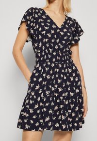 Blommig kortärmad klänning i marinblått, med V-ringning, elastisk midja och en lager-på-lager kjol med ett litet blommönster.