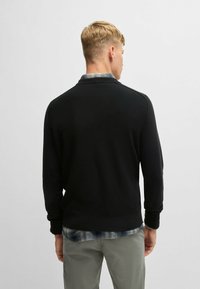 Svart, texturerad tröja med rund halsringning, ribbade ärmslut och fåll. Bärs över en rutig skjorta. Avslappnad passform, tillverkad av mjukt tyg.