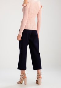 Maglione a coste rosa chiaro con spalle scoperte e dettagli a volant, abbinato a pantaloni ampi blu navy e sandali con tacco quadrato beige.