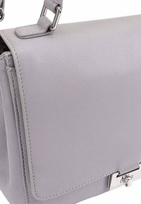 Lichtgrijze leren handtas met een gladde afwerking, klep sluiting, zilverkleurige hardware en contrasterende stiksels langs de randen.