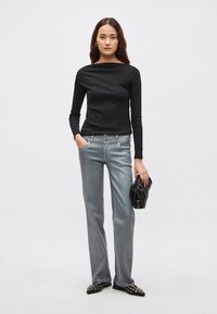 Must tekstuuriga pikkade varrukatega pluus, mida kannavad heledat halli sirge säärega teksad. Model hoiab musta, kokkupandavat käekotti. Mustad naelutatud kingad.