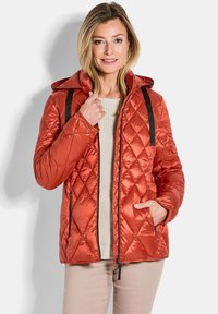 Gesteppte orange Pufferjacke mit Kapuze, ausgestattet mit schwarzen Akzentriemen und Reißverschlusstaschen. Weiche Textur und schlankes, leichtes Design.