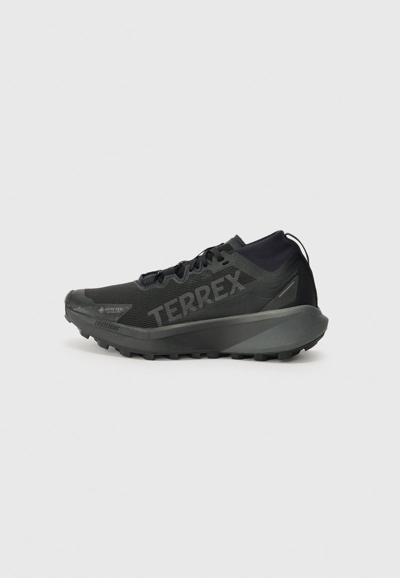 Black Terrex running shoe with a textured upper, rigid sole, and prominent branding. Features a cushioned heel for support and traction.