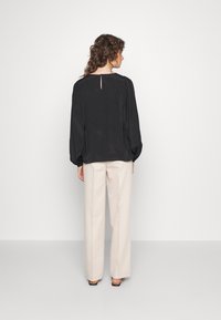 Blusa preta de manga longa com detalhe em abertura nas costas, tecido texturizado, corte relaxado, acompanhada de calças largas em bege claro.