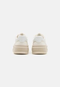 Sneakers bianchi con una parte superiore in pelle liscia e un tallone testurizzato, logo embossato sul lato e una suola spessa beige.