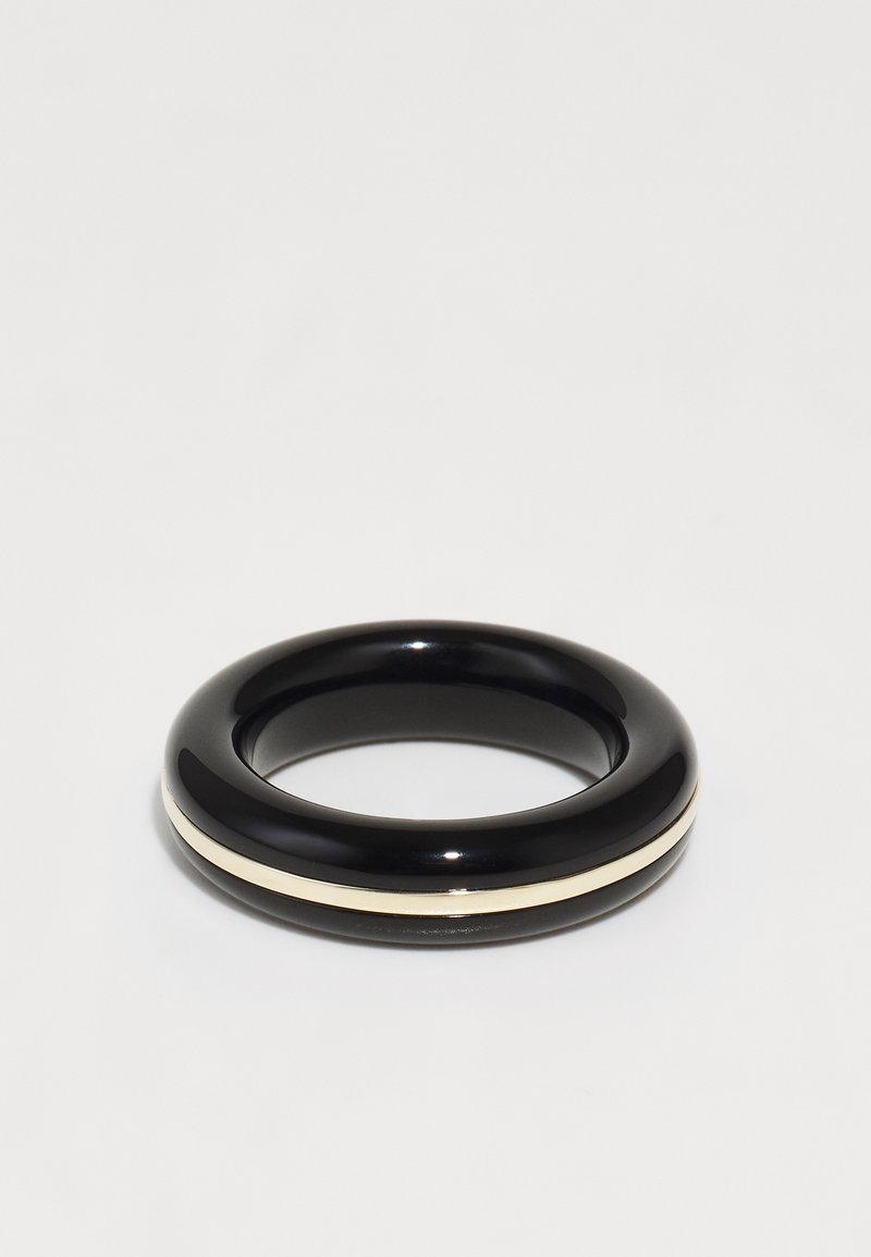 Črn sijajen bangle z gladko teksturo, ki ima ožji kremni trak okoli svoje obodnosti. Krožna, minimalistična zasnova.