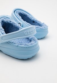 Crocs azzurri chiari con morbido rivestimento in pile blu testurizzato, cinturino regolabile e fori perforati, dotati di suola in gomma con dettagli antiscivolo.
