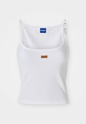 Hvid ribbet tanktop med justerbare stropper, der har et blåt logo-label og et lille brunt tag, fremstillet af blødt, strækbart materiale.