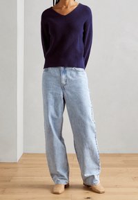 Dark navy knitted sweater with V-neck and textured chevron pattern paired with light blue wide-leg jeans and woven beige mules.