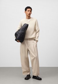 Beige knitted sweater, cream inner shirt, beige wide-leg trousers, black oversized handbag with stitching details, and black slip-on shoes.