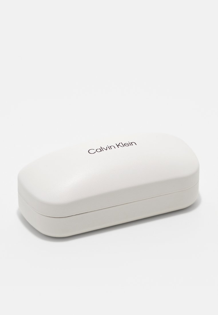 Etui na okulary Calvin Klein, z miękkiego białego plastiku, o owalnym kształcie z matowym wykończeniem, z wytłoczonym logo na górze, kompaktowe i lekkie.