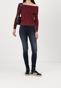 Un pull en mohair bourgogne à épaules dénudées, associé à un jean skinny noir et des baskets noires avec des rayures blanches et une semelle en caoutchouc.