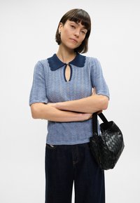 Ανοιχτό γαλάζιο πλεκτό πουλόβερ με ναυτικό γιακά και λεπτομέρεια με ανοιχτό στοίχισμα, σε συνδυασμό με ψηλόμεσα σκούρα τζιν παντελόνια και μαύρη πλεκτή τσάντα.