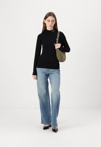 Svart langermet skjorte, lyseblå vide jeans og svarte lakksko. Holder en liten olivengrønn skulderveske.