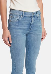 Jeans in denim azzurro chiaro con vestibilità slim, caratterizzati da un classico design a cinque tasche, un leggero sbiadimento e dettagli metallici in vita.