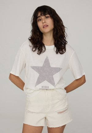 T-shirt bianca con una grande stampa di stella grigia e testo "NEVADA". Abbinata a pantaloni corti in denim bianco strappati. Vestibilità casual, tessuto morbido.