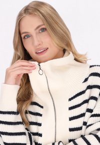 Maglione zip-up a righe bianche e nere con colletto alto e texture a coste, dotato di zip in metallo e vestibilità comoda.