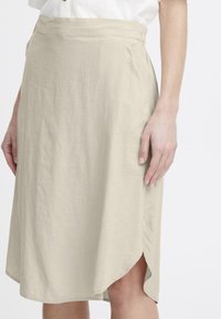 Jupe beige, longueur genou, faite d'un tissu léger. Dotée d'une fente sur le côté et d'une taille ajustée, avec une surface lisse et légèrement texturée.