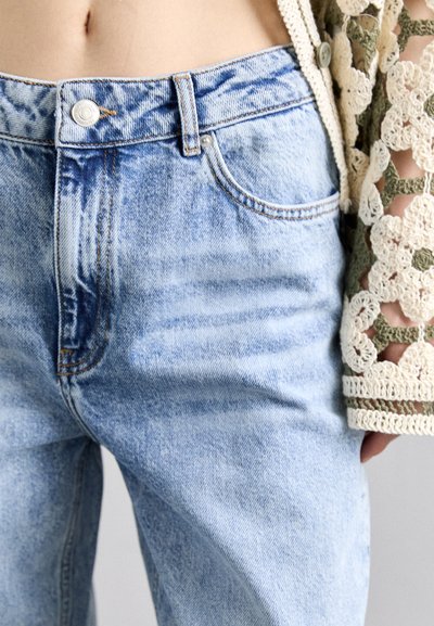 Lyseblå denimjeans med en lett falmet finish, fem lommer og knappelukking, kombinert med en kremfarget lacy heklet cardigan.