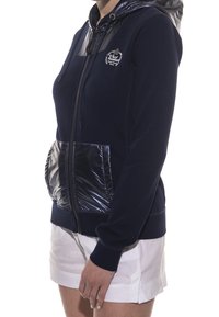 Felpa con cappuccio blu navy con una tasca frontale gonfia nera lucida, chiusura con zip e cappuccio abbinato. Presenta un logo sul petto e polsini a costine.