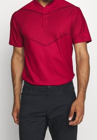 Röd kortärmad polo skjorta med en strukturerad mönster och mandarin-krage. Bärs med svarta byxor och visar en figurnära stil.