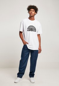 White t-shirt featuring a black rainbow graphic with the word "SOUTHPole." Paired with dark blue denim pants and white sneakers.
