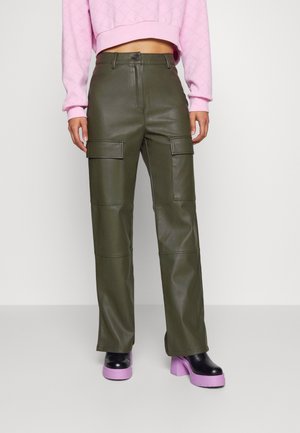 Persona que lleva pantalones cargo verde oliva, botas negras con plataforma y suela rosa, y un suéter rosa corto.
