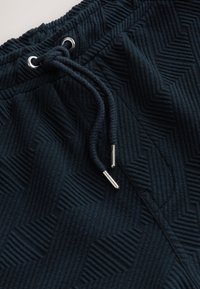 Dark blue joggers featuring a textured zigzag pattern, elastic waistband with drawstring, and metal aglets on the drawstring ends.